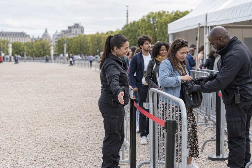Agents filtrant le public derrière des barrières à l'entrée d'un événement en plein air